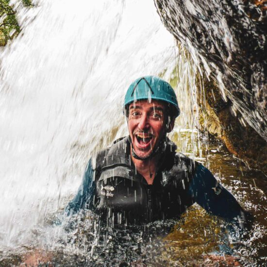 Passage d'une personne sous une cascade sur le parcours demi-journée canyoning de l'Azéro lors d'un EVG avec Nature Canyon Ardèche